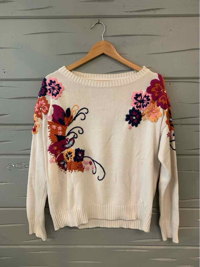 White knit sweater with colorful floral embroidery in pink, purple, and orange on the front and sleeves, featuring a relaxed