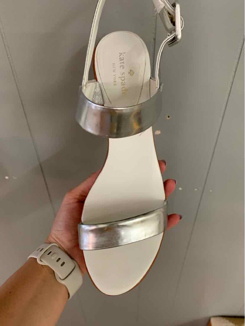 White open-toe sandal with metallic silver ankle and toe straps, flat sole, and buckle closure.