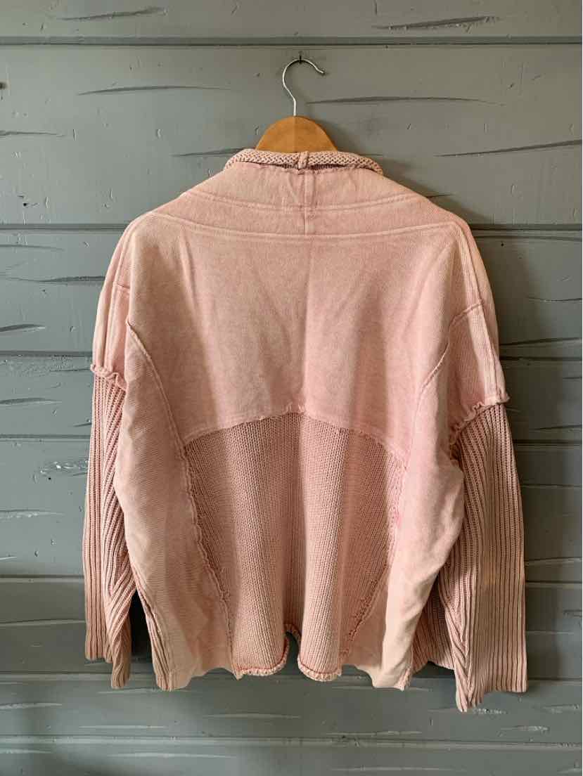 Light pink knit sweater with long sleeves and a relaxed fit hanging on a wooden hanger.