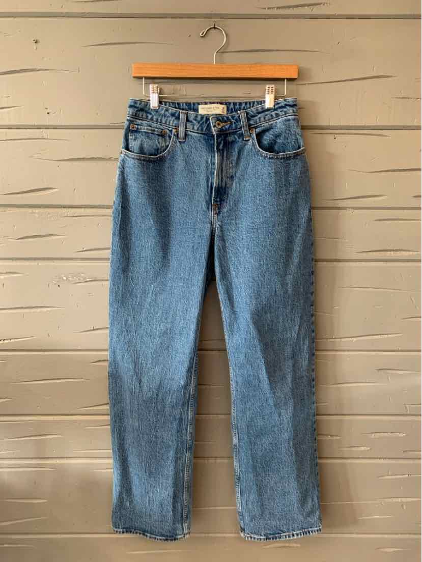 High-waisted blue denim jeans with front pockets and a straight leg cut hanging on a wooden hanger.