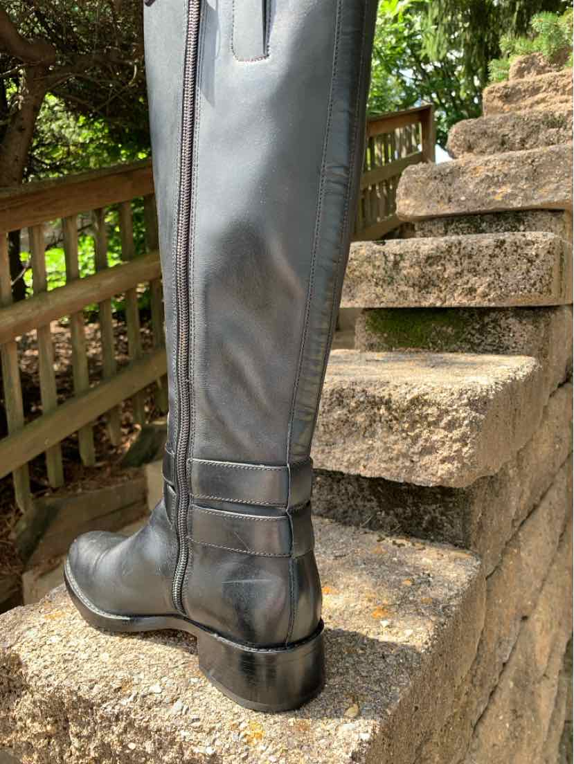 Black leather women's boot with mid-calf height and decorative strap detail at the heel.
