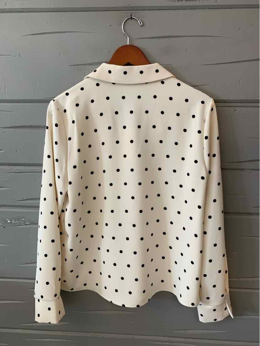 Cream long-sleeve blouse with black polka dots and a classic collar on wooden hanger.