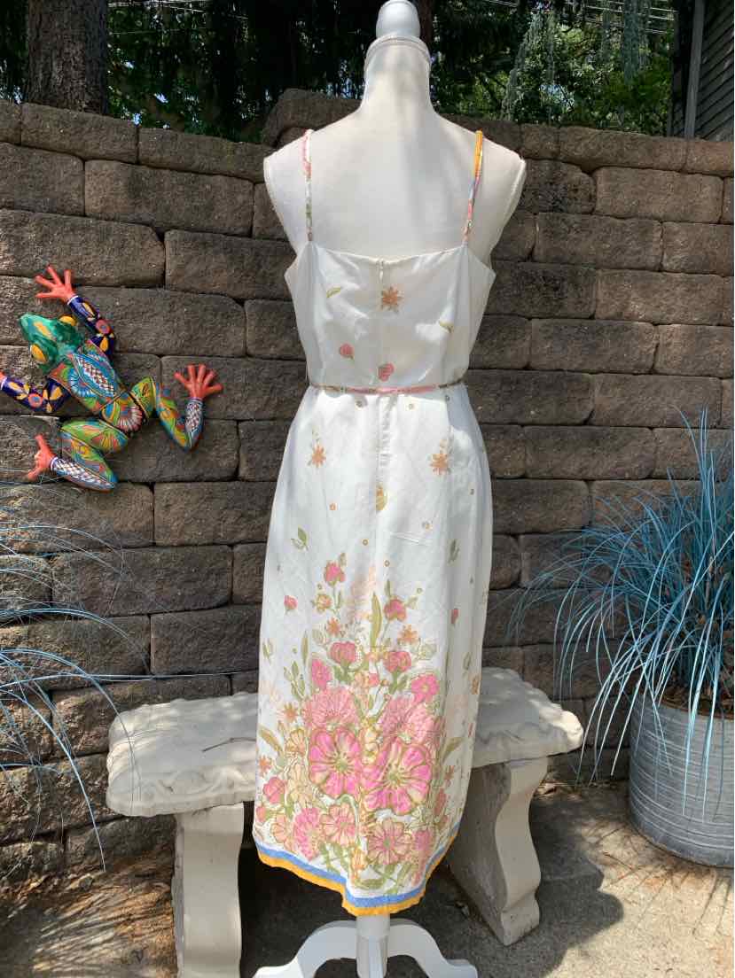 White midi dress with pink and green floral embroidery, spaghetti straps, and a scalloped hem.