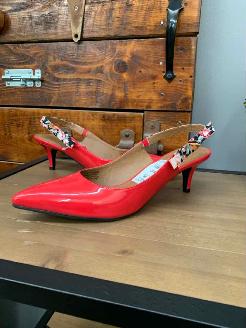Red patent leather pointed-toe slingback heels with floral ankle straps on wood surface.
