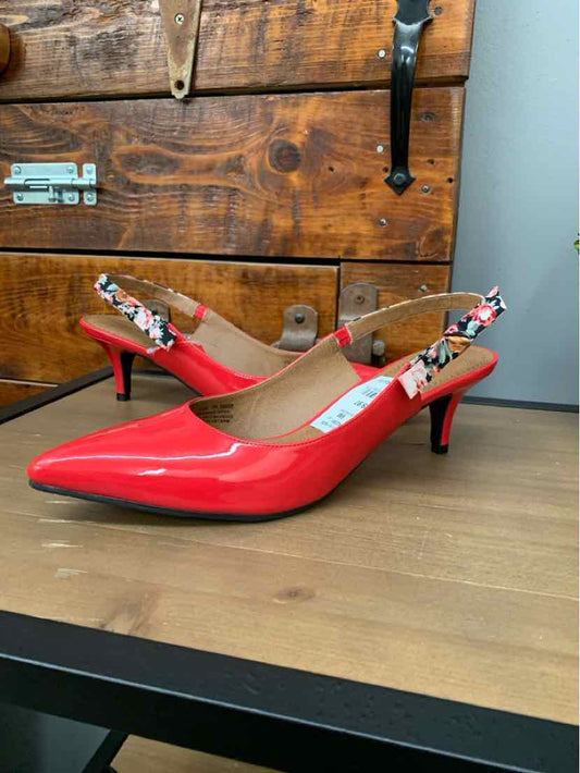 Red patent leather pointed-toe slingback heels with floral ankle straps on wood surface.