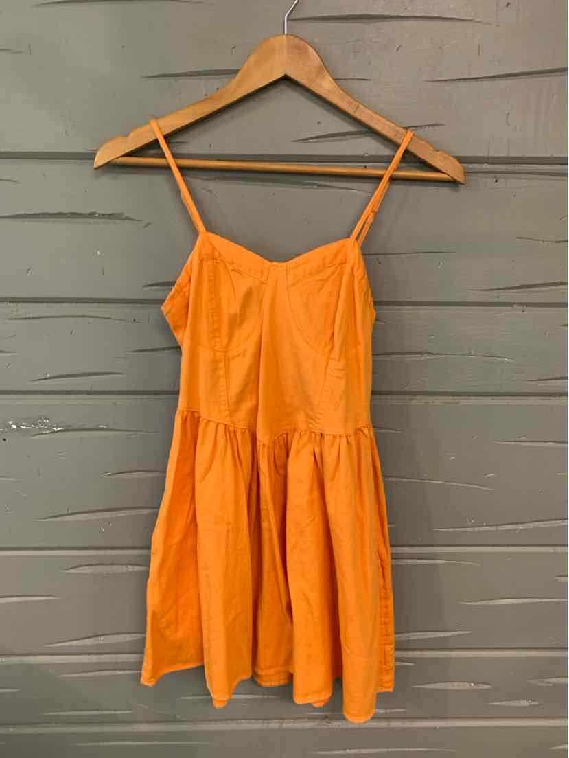 Bright orange sleeveless mini dress with thin spaghetti straps and gathered skirt on wooden hanger.