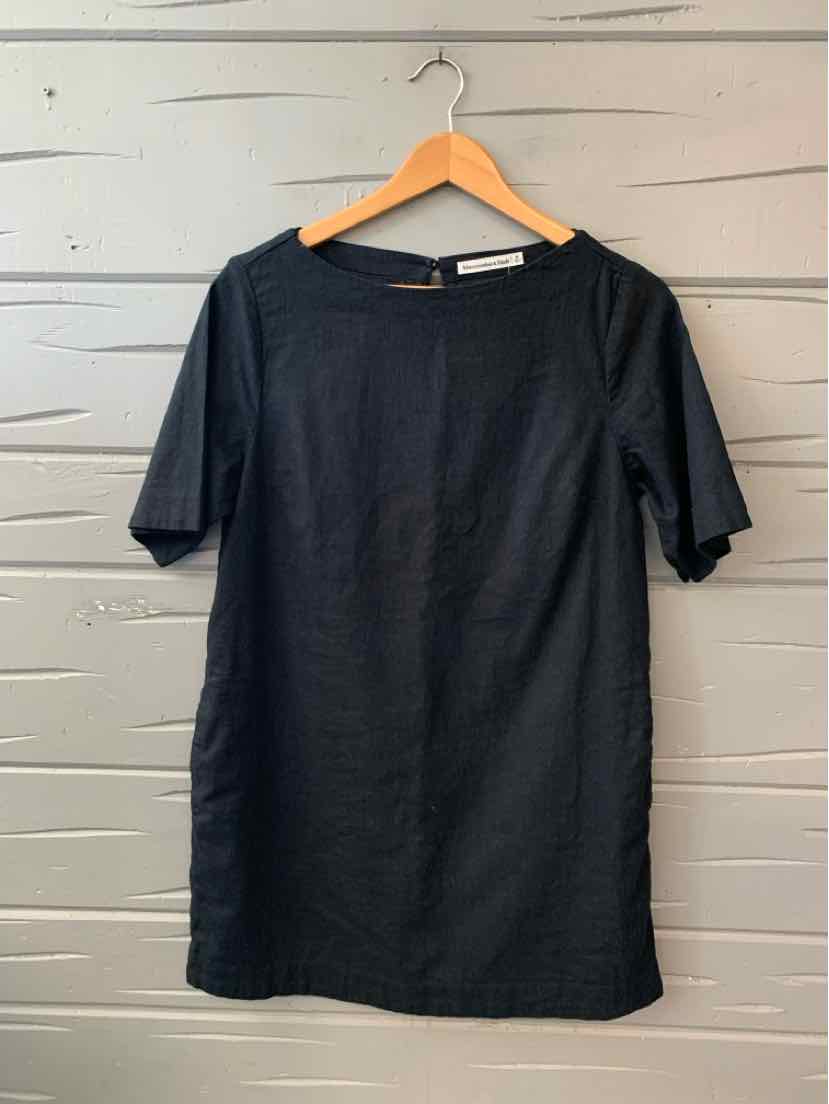 Black short-sleeve dress with a straight silhouette and round neckline hanging on wooden hanger.