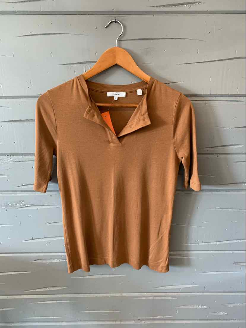 Tan short-sleeve knit top with split neckline, medium size, hanging on wooden hanger against gray wooden wall.