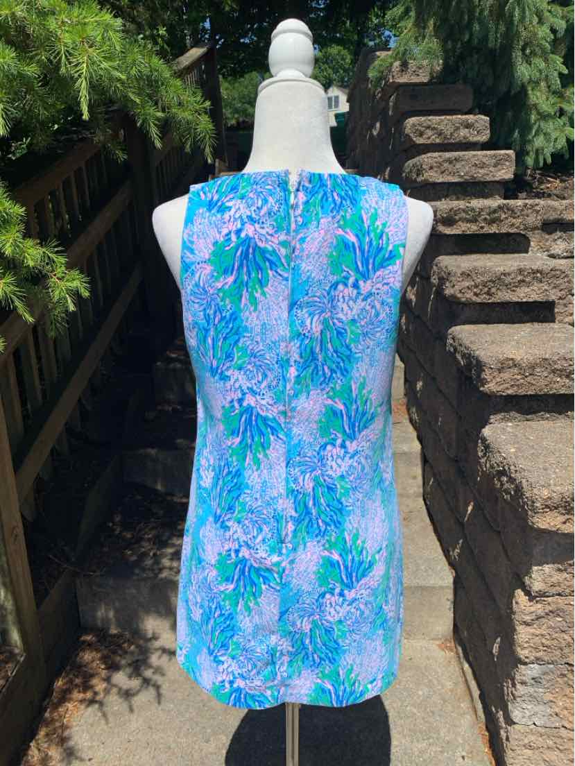 Sleeveless blue dress with green and purple tropical leaf pattern, knee-length, fitted silhouette.
