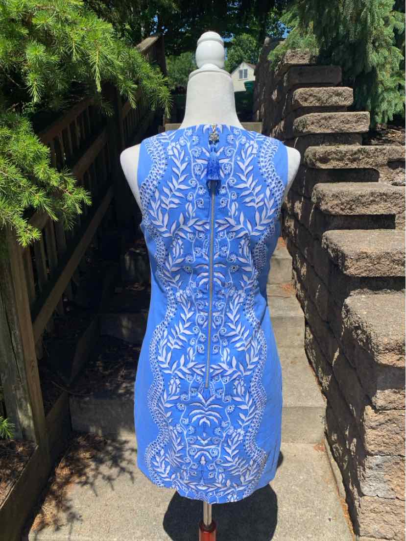 Blue sleeveless knee-length dress with white floral leaf pattern, fitted silhouette.
