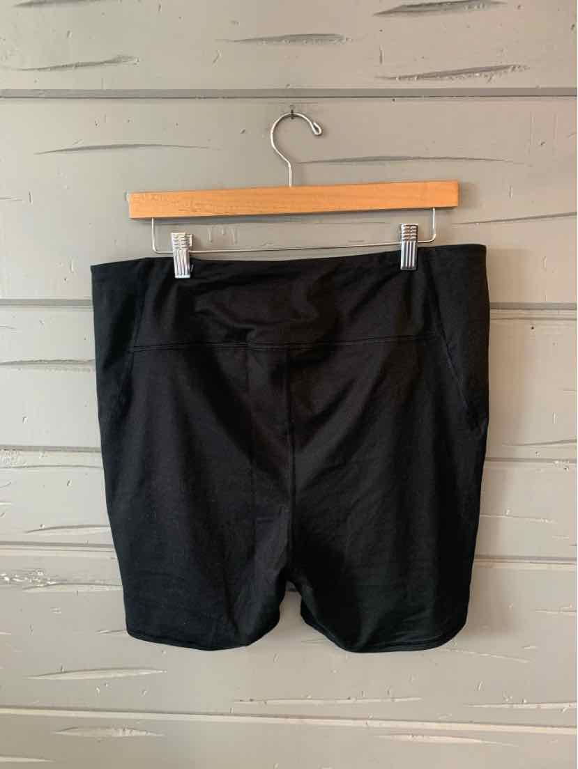 Black knee-length shorts with a fitted waist, hanging on a wooden hanger against a white wall.