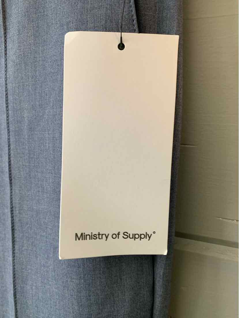 White Ministry of Supply clothing tag hanging on gray fabric background.