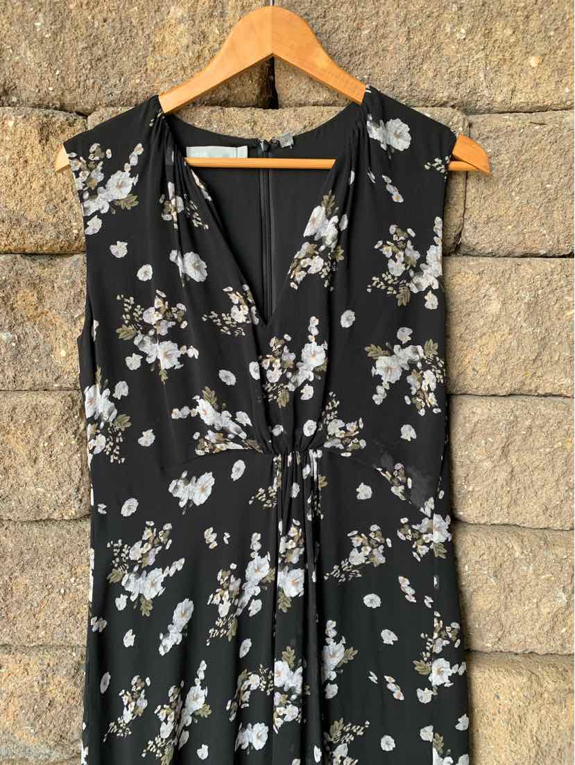 Black sleeveless blouse with white floral print and front tie detail on wooden hanger.
