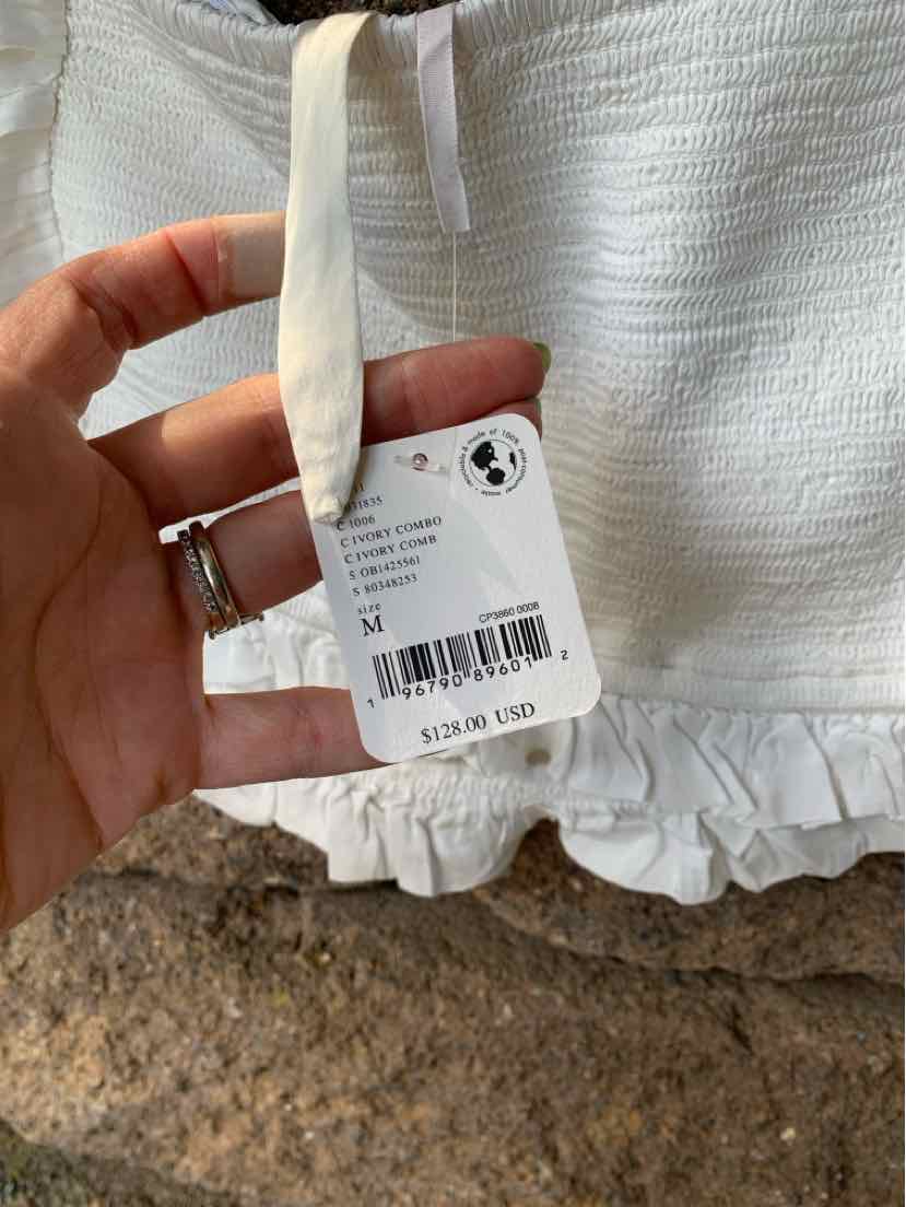 White textured fabric top with ruffle hem and adjustable shoulder tie strap, size medium tag visible.