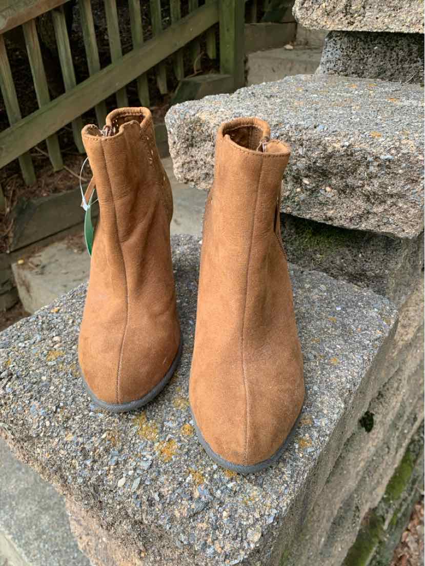 Tan suede ankle boots with rounded toes and pull tabs on a stone surface.