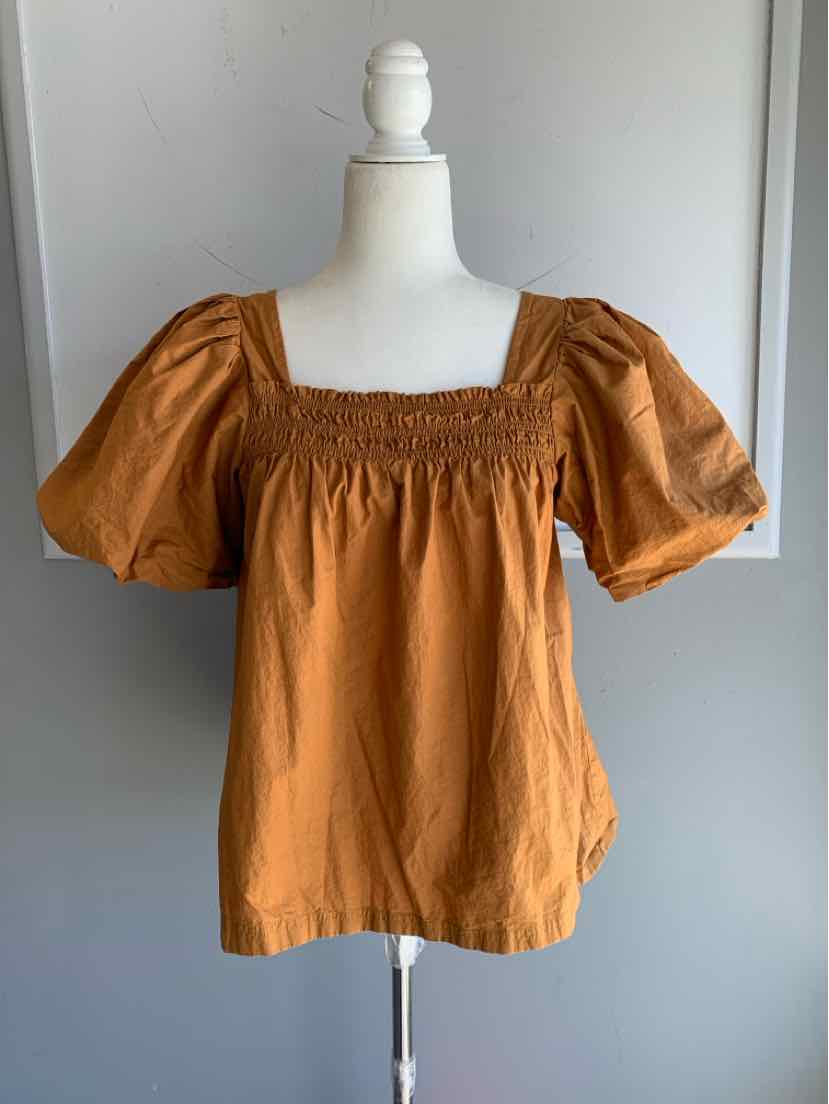 Tan short-sleeve blouse with smocked square neckline and puffed sleeves on mannequin.