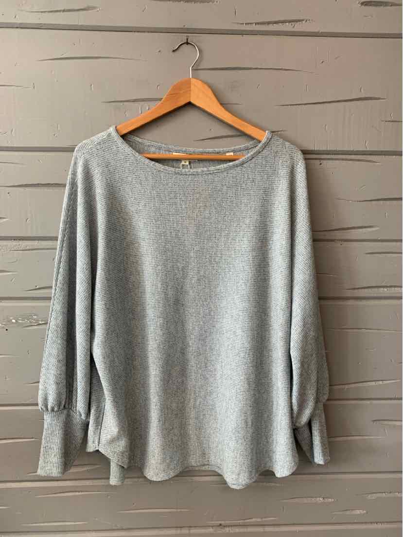 Light gray long-sleeve sweater with relaxed fit and ribbed cuffs on wooden hanger.