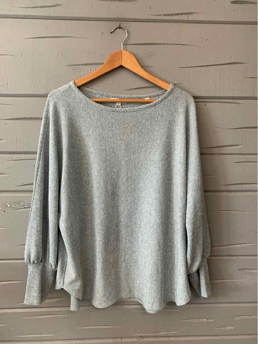 Light gray long-sleeve sweater with relaxed fit and ribbed cuffs on wooden hanger.