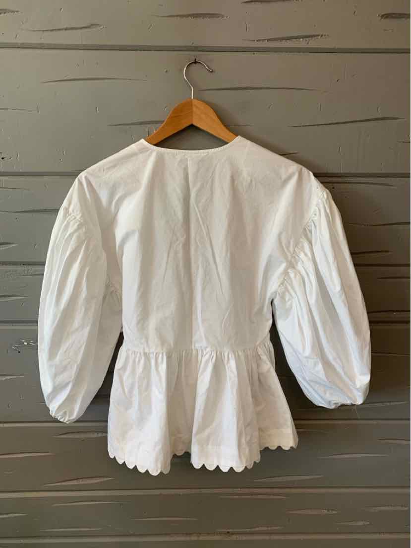 White long-sleeve blouse with gathered waist and puffed sleeves hanging on wooden hanger.