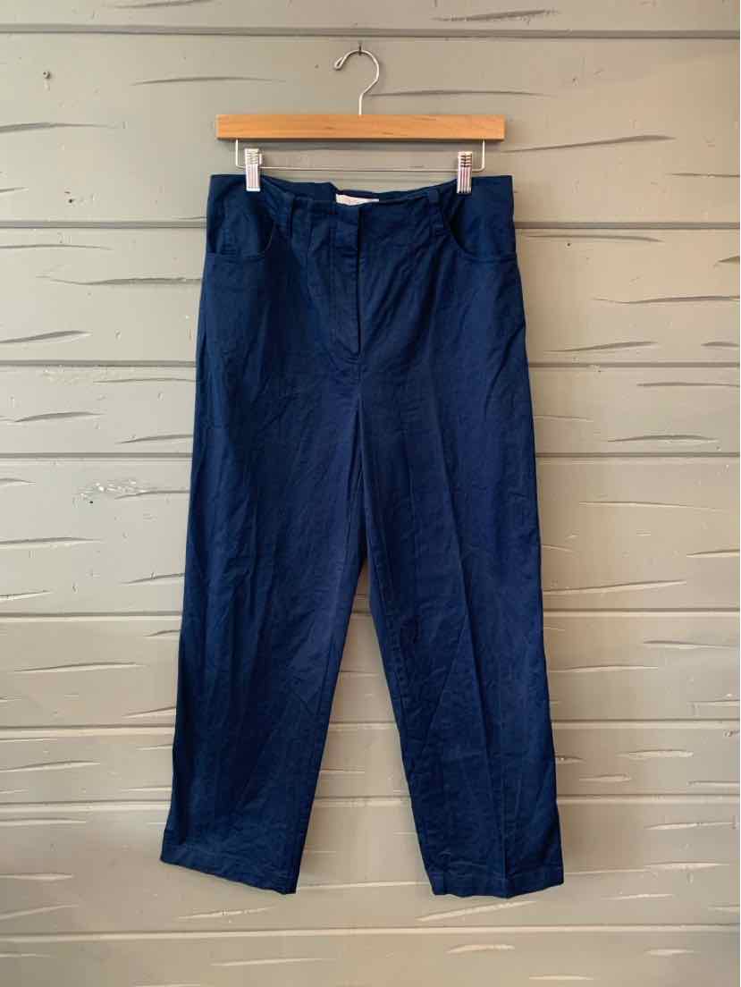 Navy blue high-waisted trousers with belt loops and front pockets hanging on wooden hanger against light wood panel.