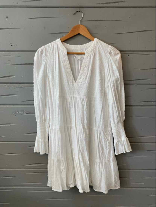 White long-sleeve dress with v-neckline, gathered fabric details, and tiered skirt on wooden hanger.