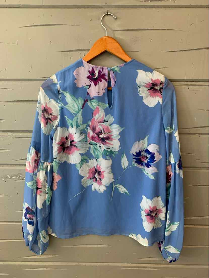 Light blue floral blouse with long puff sleeves and button cuffs on wooden hanger.