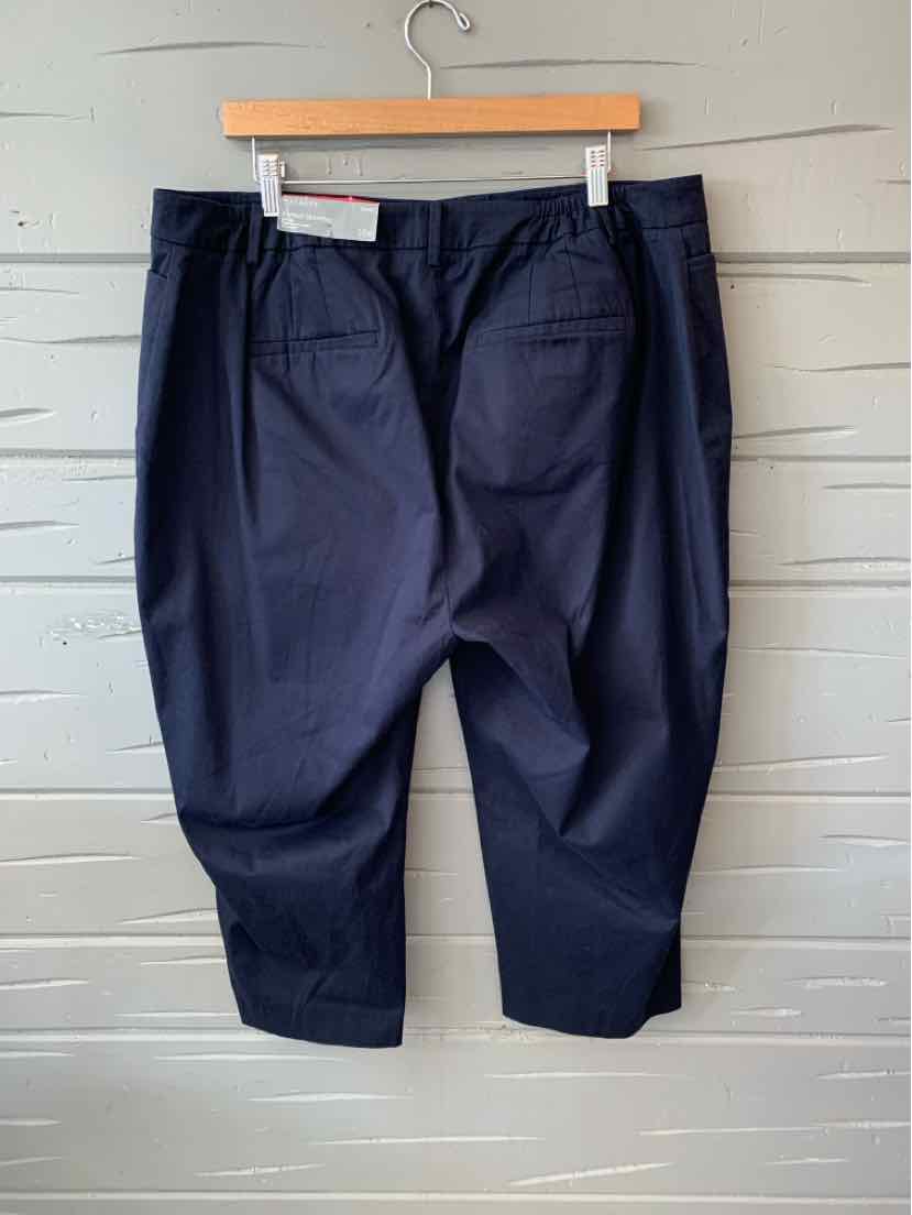 Navy blue wide-leg trousers with back pockets hanging on wooden hanger against gray wall.