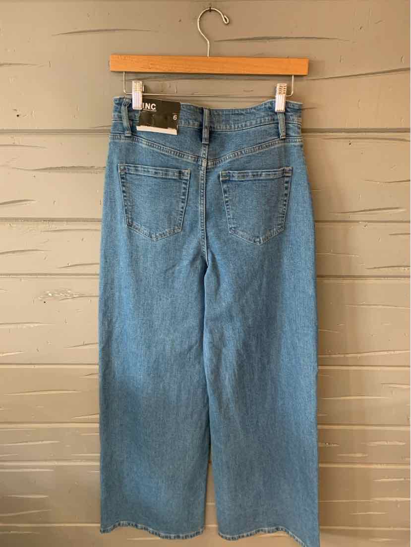 Light blue denim jeans in size 6 with a high waist and wide legs hanging on a wooden hanger.