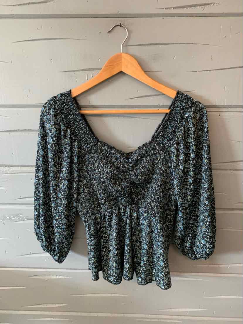 Black floral long-sleeve blouse with ruched bodice and peplum hem on wooden hanger.