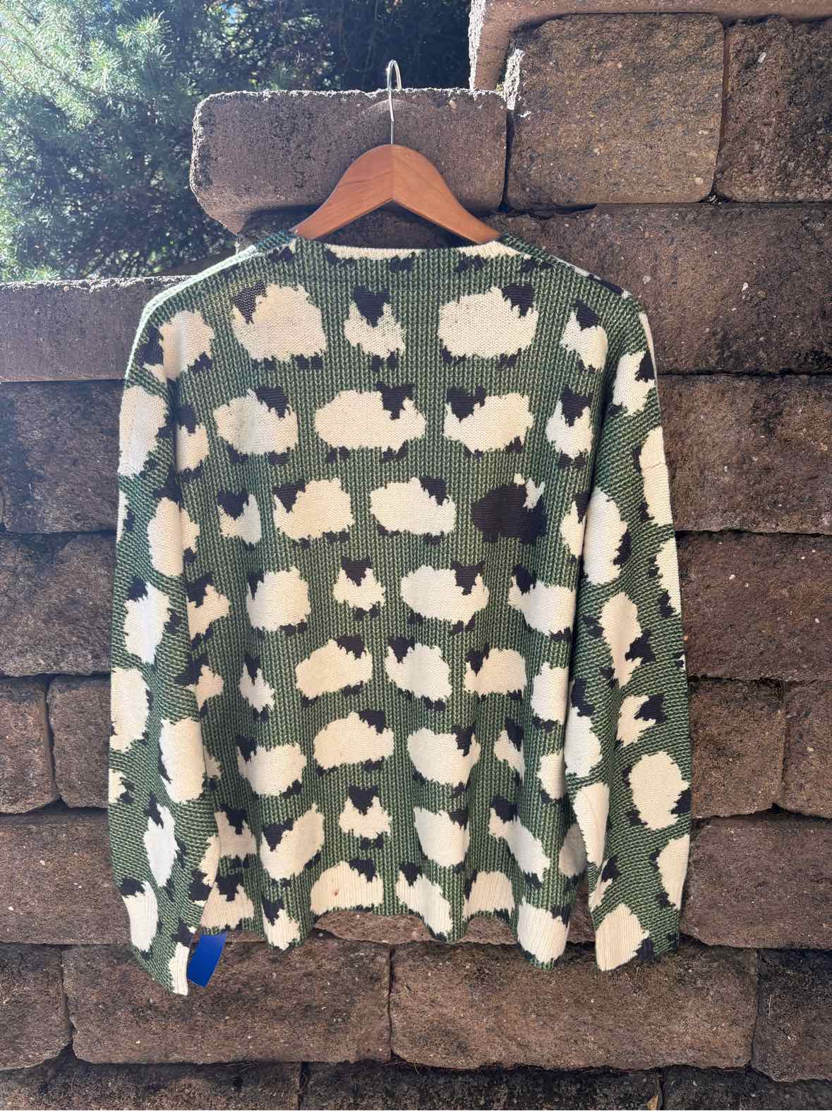 Green knit sweater with a repeating white sheep pattern and a dark ribbed crew neckline.