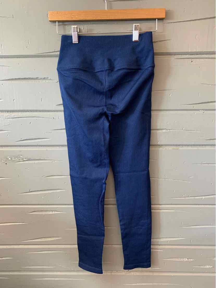 Navy blue ribbed knit high-waist leggings hanging on wooden hanger against gray paneled wall.