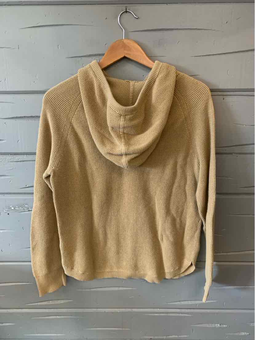 Tan hoodie with long sleeves and a relaxed fit hanging on wooden hanger against gray wall.