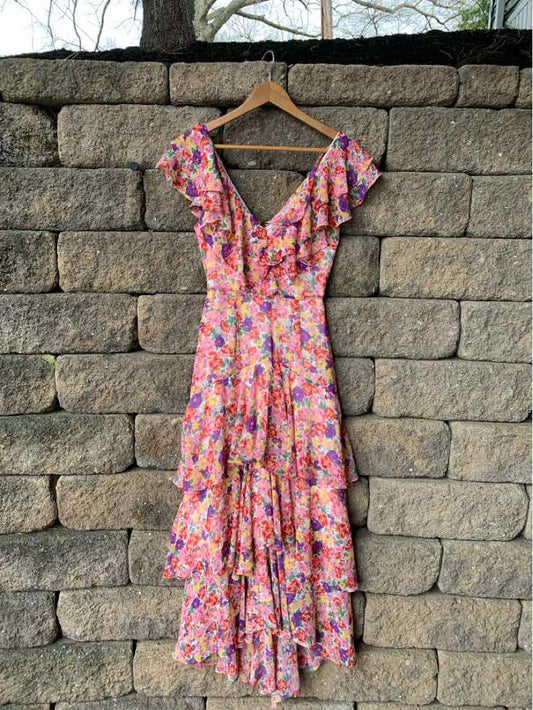 Floral multi-color tiered maxi dress with short ruffled sleeves and V-neckline on wood hanger against stone wall.