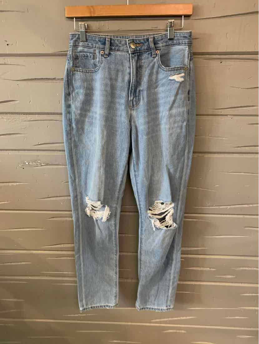 Light blue distressed denim jeans with ripped knees and classic five-pocket design hanging on wooden hanger.