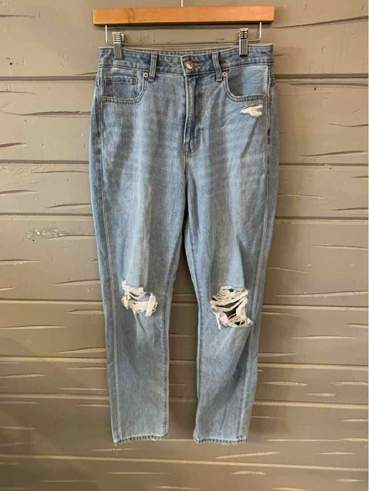 Light blue distressed denim jeans with ripped knees and classic five-pocket design hanging on wooden hanger.