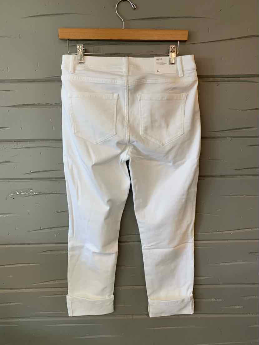 Cropped white denim jeans with rolled cuffs and back pockets hanging on wooden hanger against gray wall.