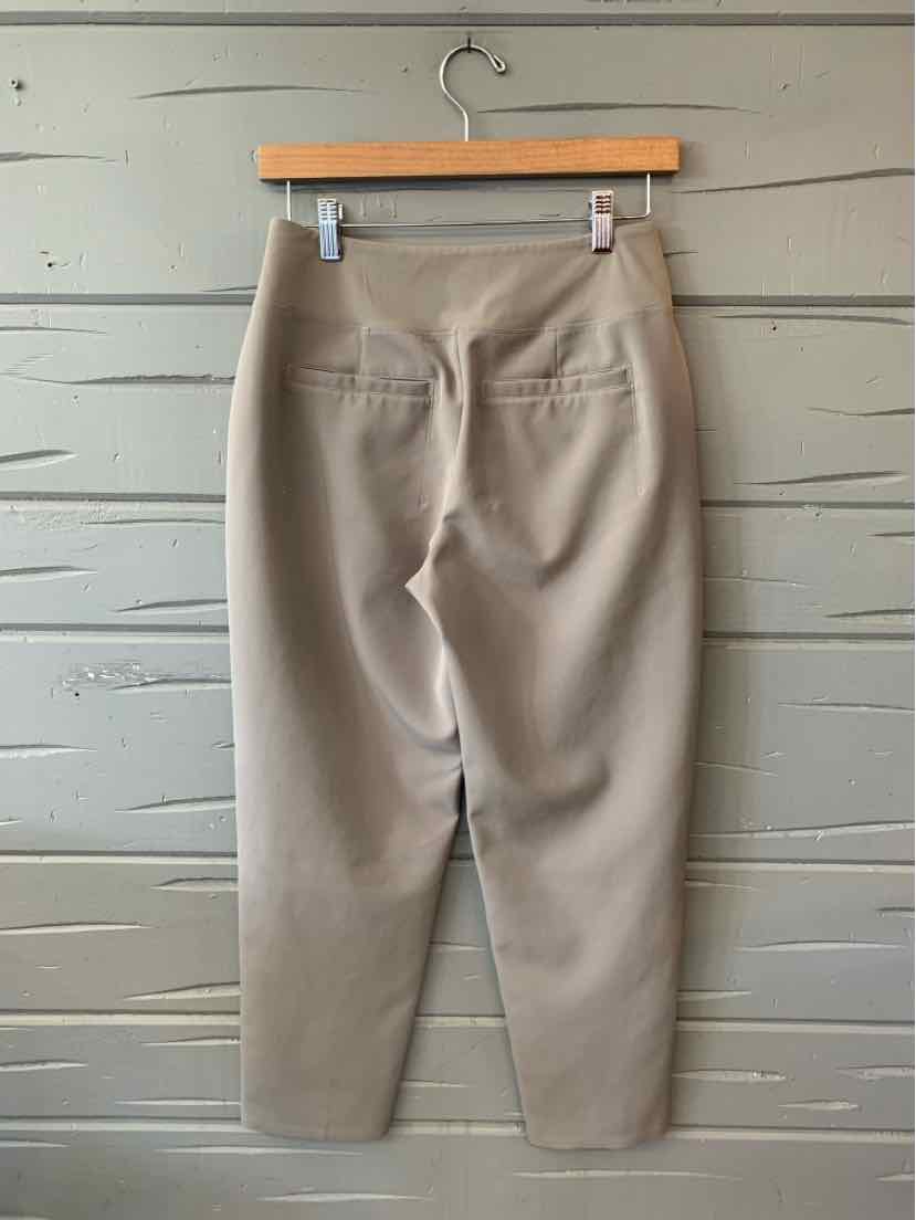 Beige high-waist tapered pants with back welt pockets hanging on wooden hanger.