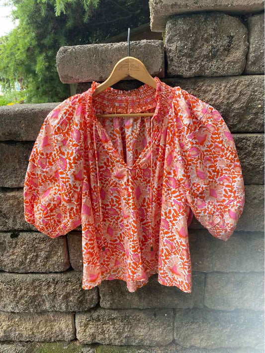 Lightweight blouse with orange, pink, and white floral pattern, puffed elbow-length sleeves, and V-neckline.