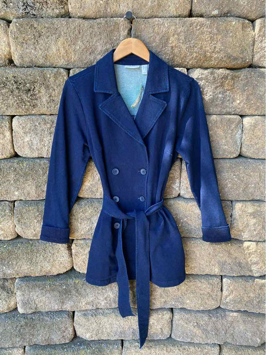 Navy blue double-breasted blazer with belt and notched collar hanging against stone wall.