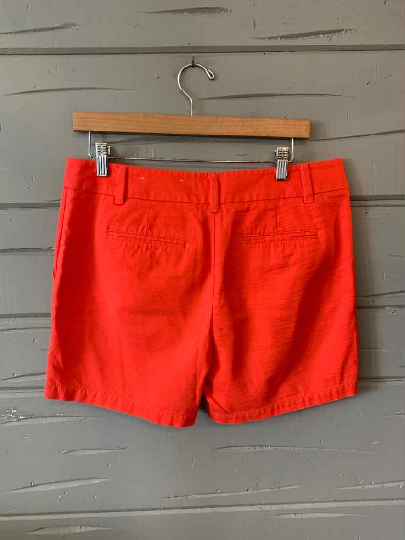 Bright red women's shorts with back pockets and a fitted waistband hanging on wooden hanger.
