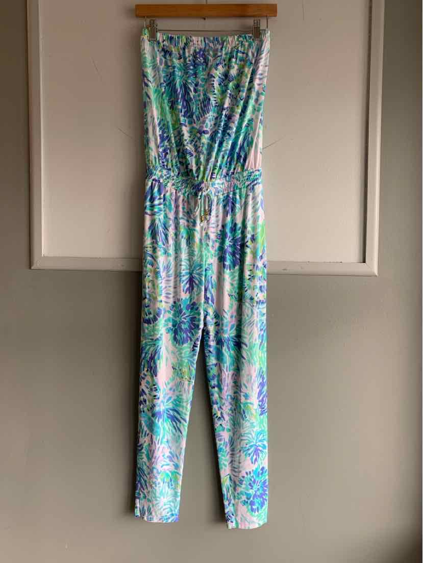 Teal tropical print sleeveless jumpsuit with gathered waist and straight legs hanging on wooden hanger.