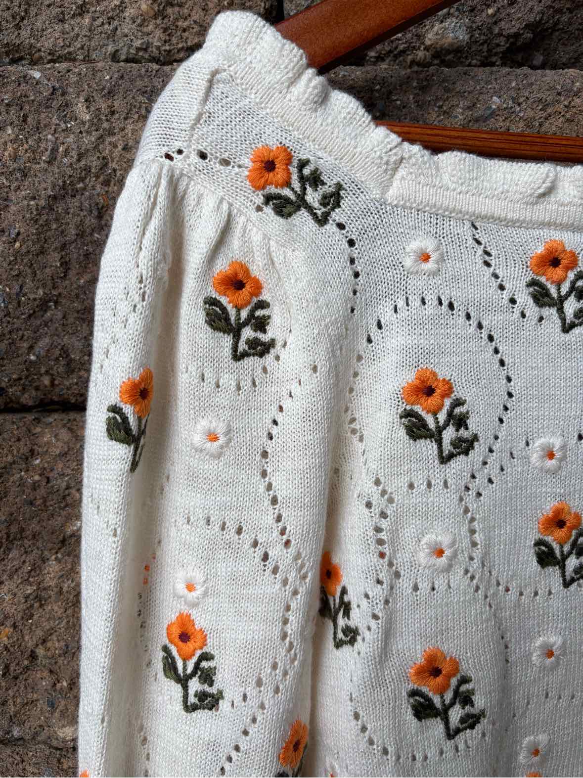 White floral eyelet fabric with orange flowers and green leaves, finished with a scalloped edge.