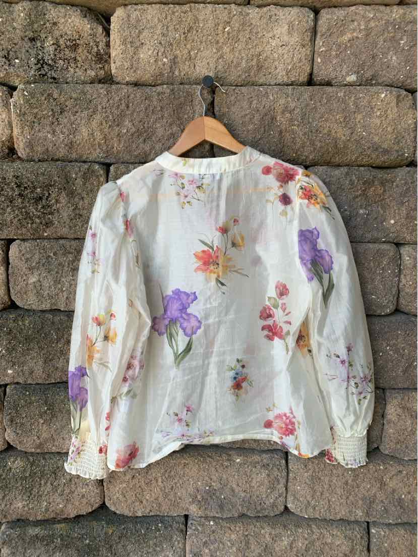 White long-sleeve blouse with colorful floral prints in orange, purple, and pink, lightweight fabric.