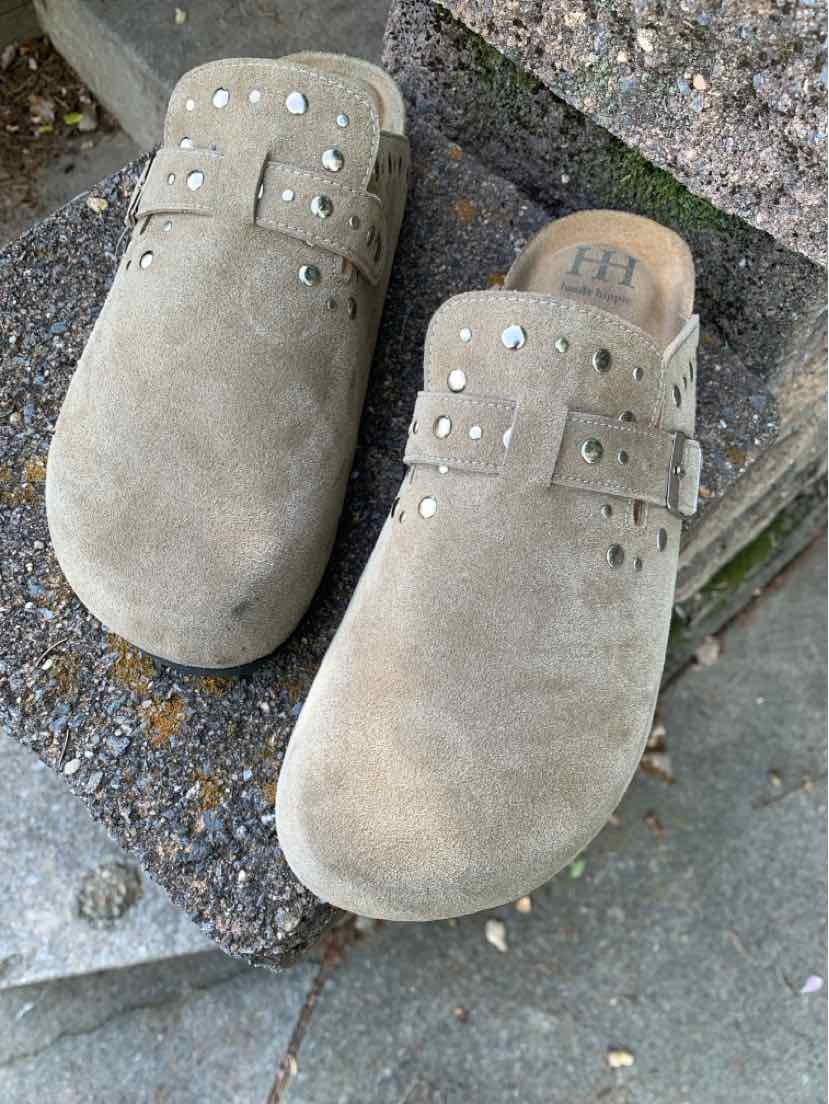 Pair of beige suede slip-on clogs with rounded toes, studded straps, and wooden soles.