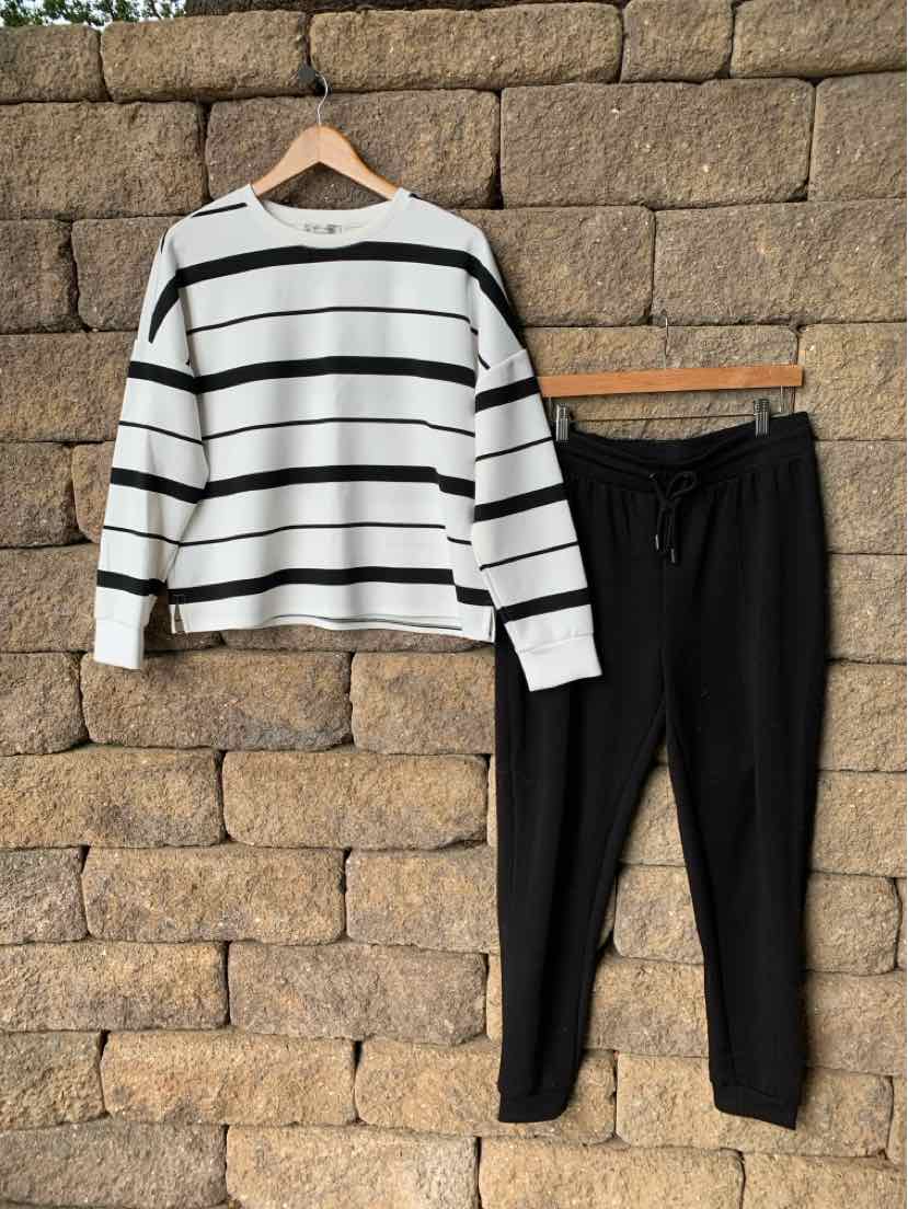 White long-sleeve shirt with black horizontal stripes paired with black jogger pants on hangers against stone wall.