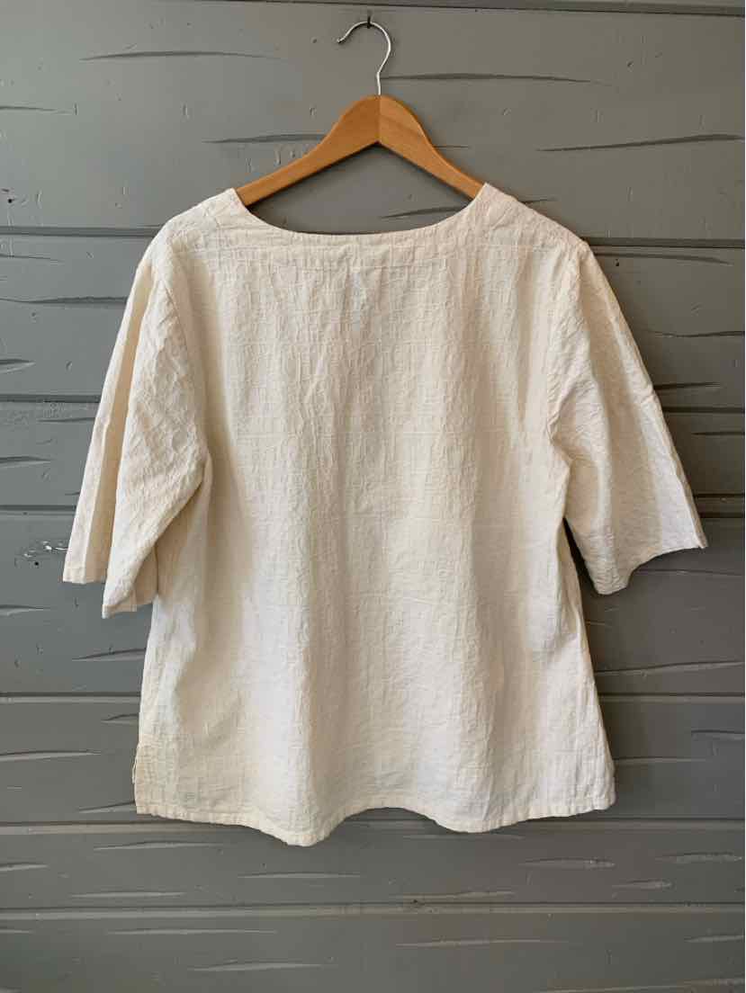 Cream-colored, loose-fit blouse with elbow-length sleeves and round neckline on wooden hanger.