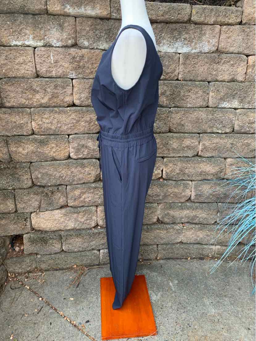 Navy blue sleeveless jumpsuit with cinched elastic waist and tapered legs on mannequin against stone wall.