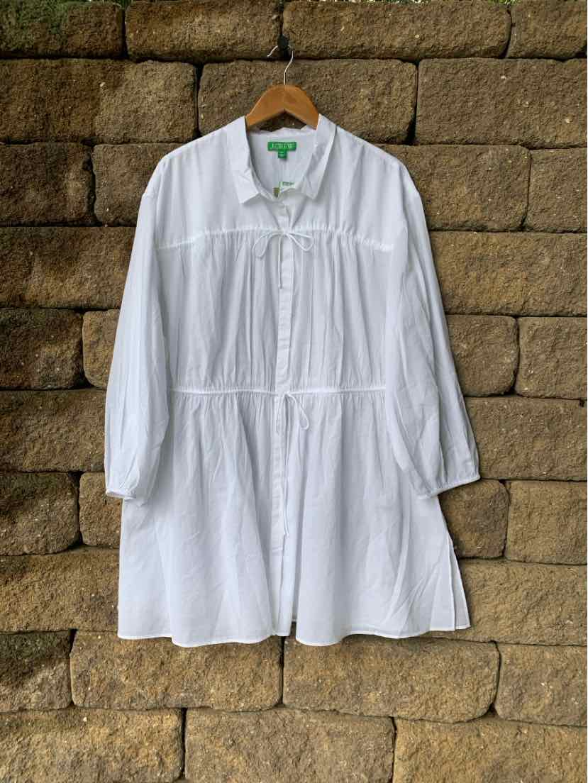 White long-sleeve, knee-length tunic dress with gathered yoke and tie neckline on wooden hanger.