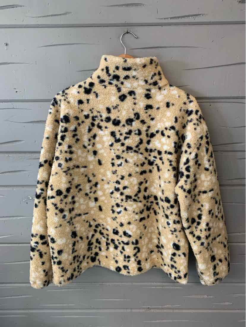 Beige and black spotted faux fur jacket with high collar and long sleeves hanging on wooden wall.