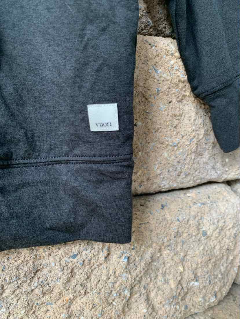 Charcoal gray VUORI sweatshirt with ribbed cuffs and a small white rectangular logo patch near the hem.